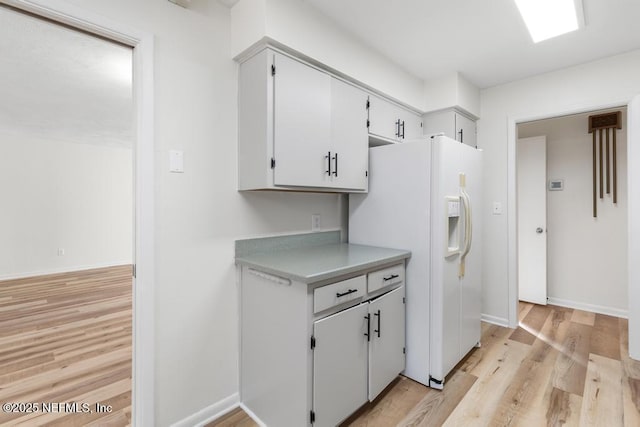 kitchen with white cabinetry, white fridge with ice dispenser, and light hardwood / wood-style flooring