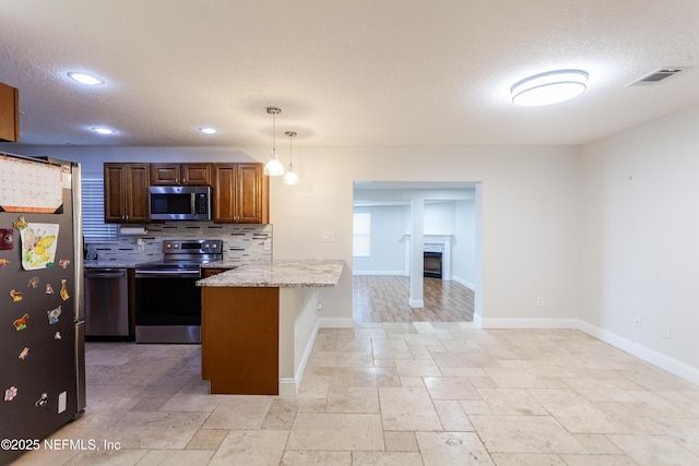 kitchen featuring pendant lighting, appliances with stainless steel finishes, tasteful backsplash, light stone counters, and kitchen peninsula