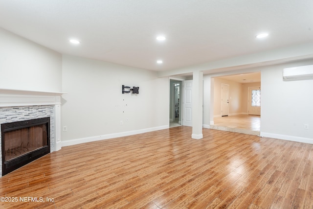 unfurnished living room with an AC wall unit, a fireplace, and light wood-type flooring