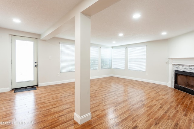 unfurnished living room with a textured ceiling, light hardwood / wood-style floors, a stone fireplace, and a wealth of natural light