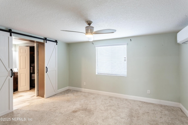 carpeted spare room with a wall mounted air conditioner, a textured ceiling, a barn door, and ceiling fan