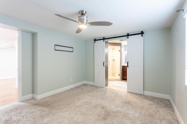 unfurnished bedroom with light carpet, ceiling fan, a barn door, a textured ceiling, and connected bathroom