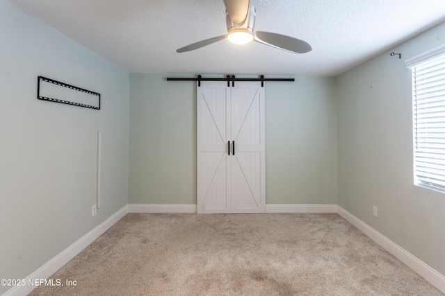 unfurnished bedroom featuring a textured ceiling, ceiling fan, a barn door, and light carpet