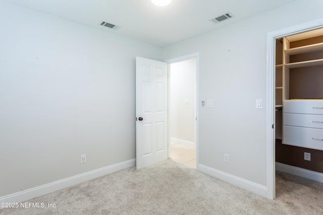 unfurnished bedroom with a spacious closet, light carpet, and a closet