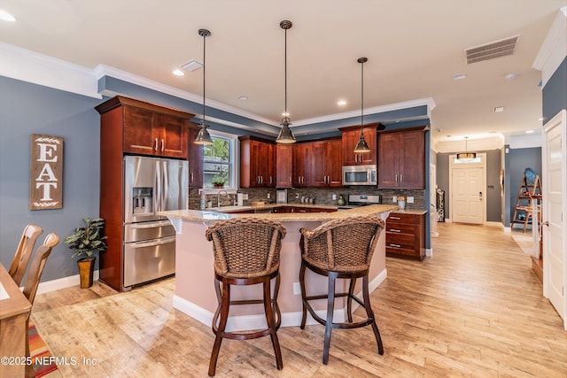 kitchen featuring appliances with stainless steel finishes, a kitchen island, hanging light fixtures, and light stone countertops