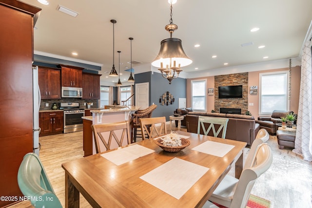 dining room featuring a healthy amount of sunlight, a stone fireplace, light wood-type flooring, and ornamental molding