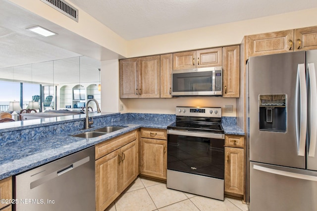 kitchen featuring sink, light tile patterned floors, dark stone counters, and appliances with stainless steel finishes