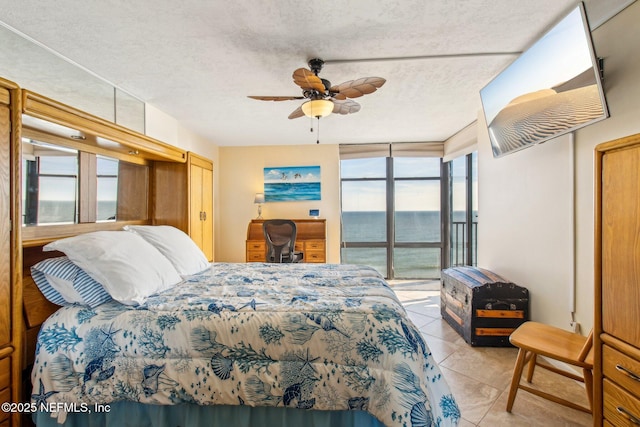 tiled bedroom with ceiling fan, a water view, and a textured ceiling