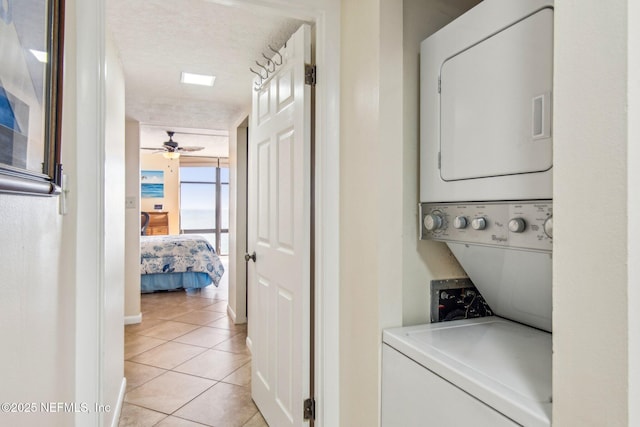 laundry area featuring ceiling fan, light tile patterned flooring, stacked washing maching and dryer, and a textured ceiling