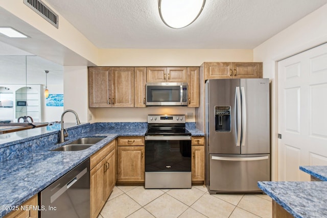 kitchen with sink, dark stone countertops, a textured ceiling, light tile patterned flooring, and stainless steel appliances