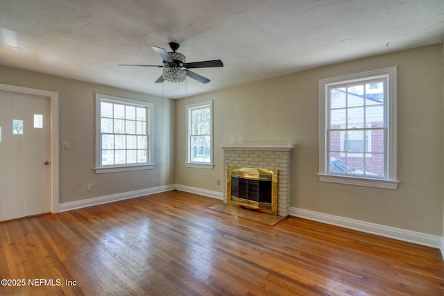 unfurnished living room featuring hardwood / wood-style floors, ceiling fan, a wealth of natural light, and a brick fireplace