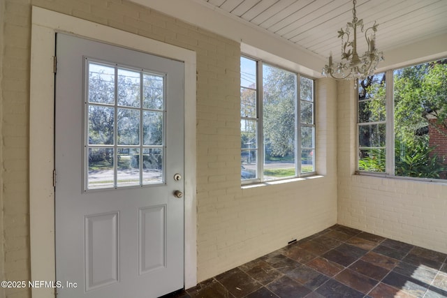 doorway with a notable chandelier, plenty of natural light, and brick wall