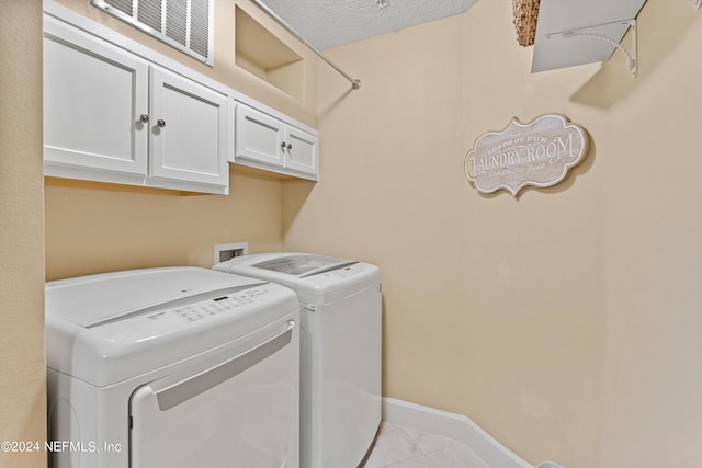 laundry room featuring cabinets, light tile patterned floors, a textured ceiling, and separate washer and dryer