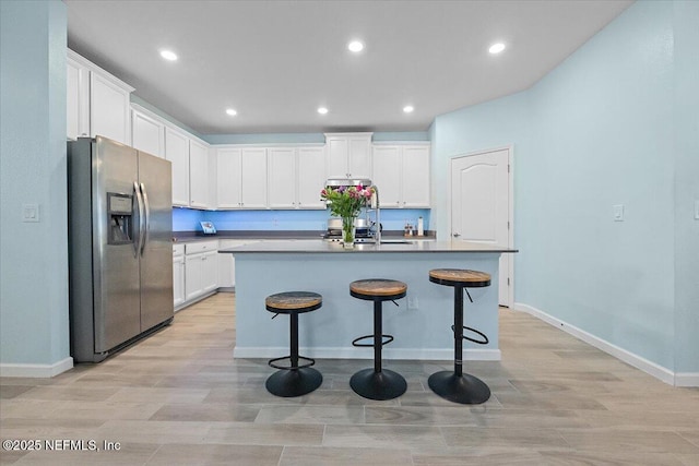 kitchen featuring white cabinetry, stainless steel refrigerator with ice dispenser, an island with sink, light hardwood / wood-style floors, and a breakfast bar