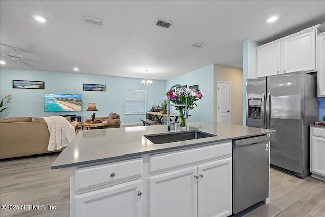 kitchen with ceiling fan with notable chandelier, stainless steel appliances, a kitchen island with sink, sink, and white cabinets