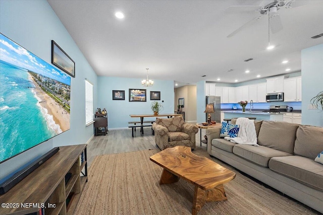 living room with ceiling fan with notable chandelier, light hardwood / wood-style flooring, and sink