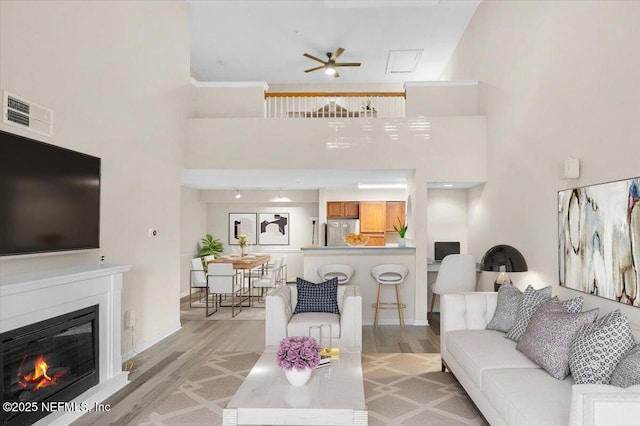 living room featuring light wood-type flooring, a towering ceiling, and ceiling fan