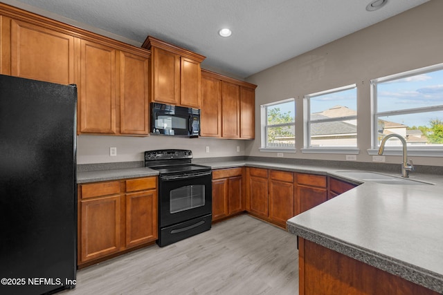 kitchen with a healthy amount of sunlight, sink, black appliances, and light hardwood / wood-style floors