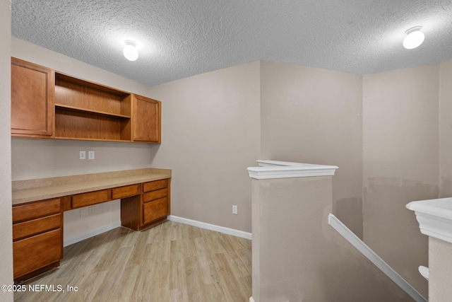 unfurnished office with built in desk, a textured ceiling, and light hardwood / wood-style flooring