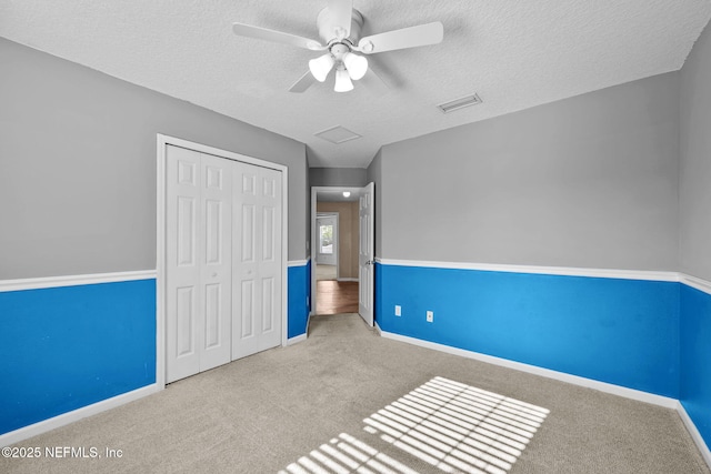 unfurnished bedroom with ceiling fan, light colored carpet, a textured ceiling, and a closet