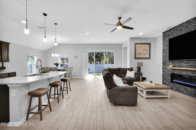 living room with ceiling fan with notable chandelier, a healthy amount of sunlight, a stone fireplace, and sink