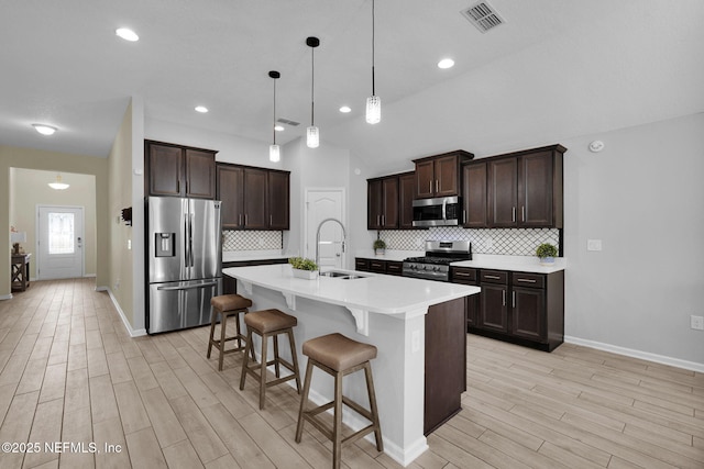 kitchen with pendant lighting, sink, an island with sink, appliances with stainless steel finishes, and a kitchen bar