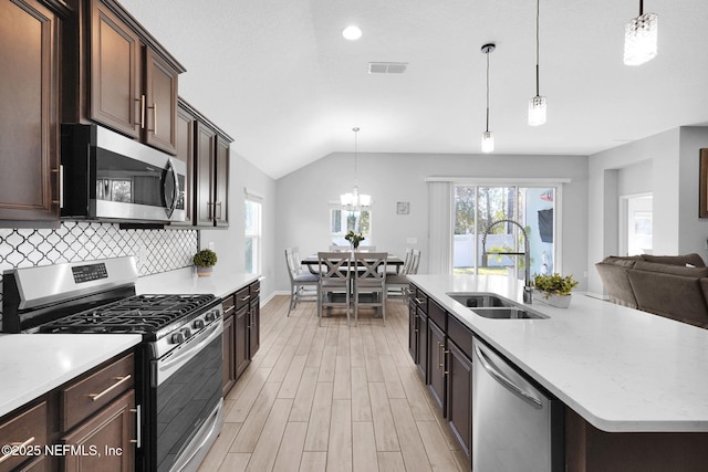 kitchen featuring appliances with stainless steel finishes, backsplash, vaulted ceiling, sink, and decorative light fixtures