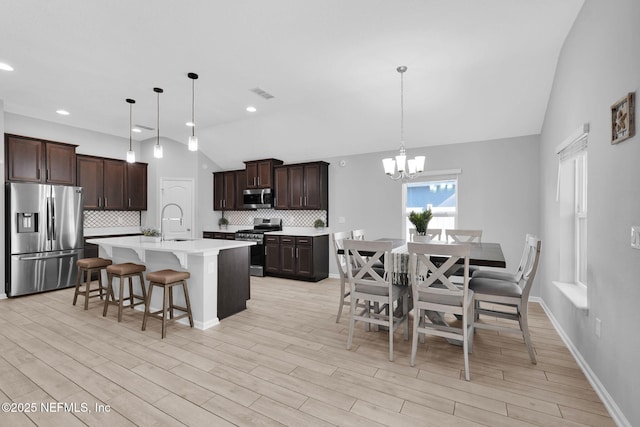 kitchen with lofted ceiling, sink, hanging light fixtures, appliances with stainless steel finishes, and tasteful backsplash