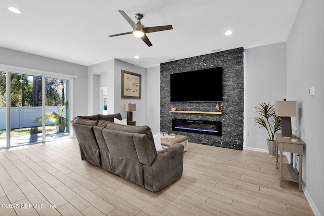 living room featuring light hardwood / wood-style flooring, a stone fireplace, and ceiling fan