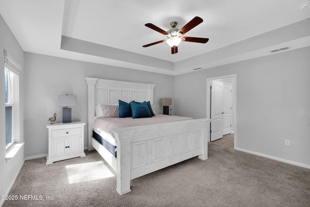 carpeted bedroom featuring a raised ceiling and ceiling fan