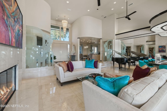 living room featuring a premium fireplace, ceiling fan with notable chandelier, and a high ceiling