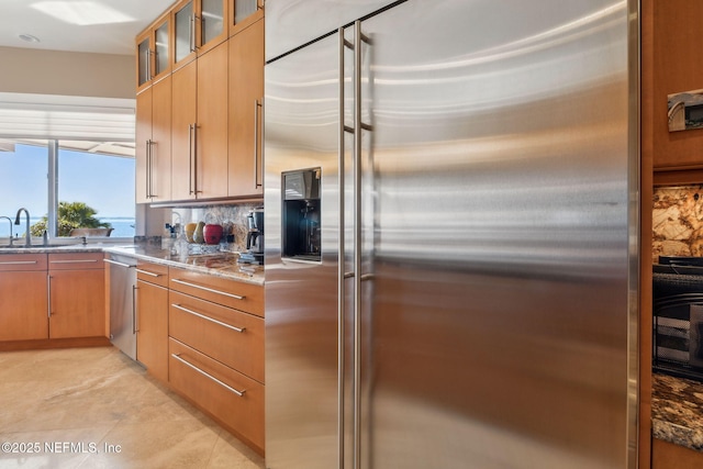 kitchen with appliances with stainless steel finishes, sink, backsplash, stone countertops, and light tile patterned floors