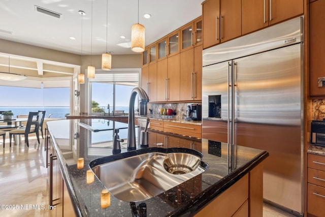 kitchen featuring decorative backsplash, sink, stainless steel built in fridge, a water view, and dark stone counters