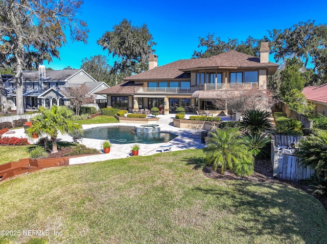 rear view of property featuring a swimming pool with hot tub, a lawn, and a balcony