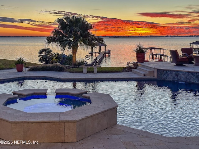 pool at dusk with a water view and an in ground hot tub