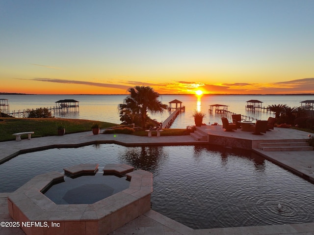 pool at dusk with an in ground hot tub and a water view