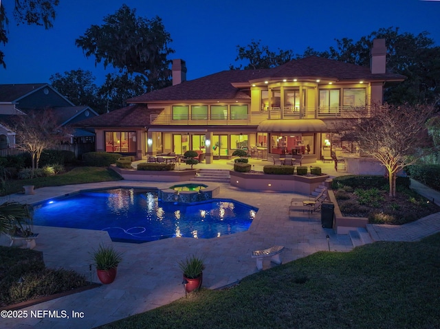 pool at twilight featuring a patio area and an in ground hot tub