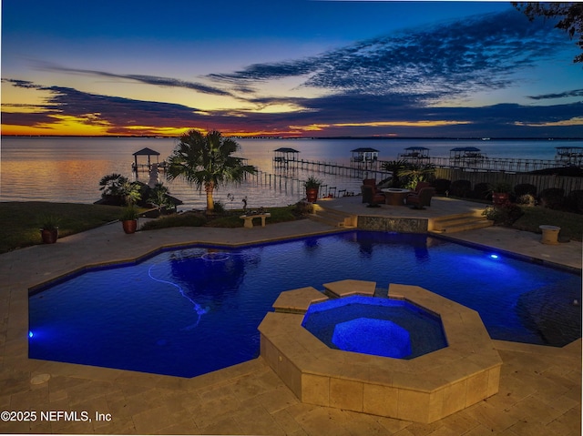 pool at dusk with a water view, a patio area, and an in ground hot tub