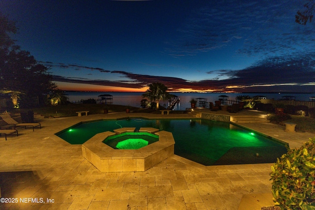 pool at dusk with a water view, a patio area, and an in ground hot tub