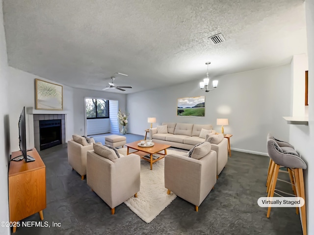 living room with ceiling fan with notable chandelier, dark carpet, a textured ceiling, and a tiled fireplace