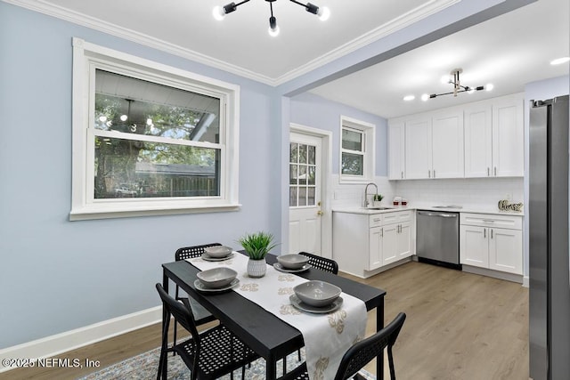 dining area featuring sink, light hardwood / wood-style flooring, an inviting chandelier, and crown molding