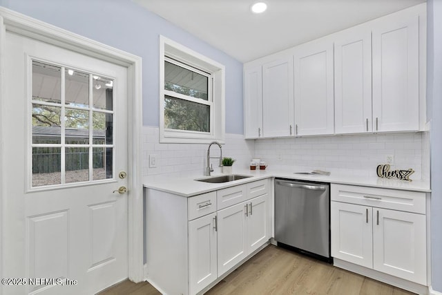 kitchen featuring dishwasher, sink, white cabinetry, light hardwood / wood-style floors, and decorative backsplash