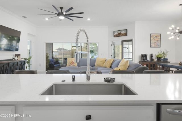 kitchen featuring light stone countertops, white cabinetry, ceiling fan with notable chandelier, ornamental molding, and sink