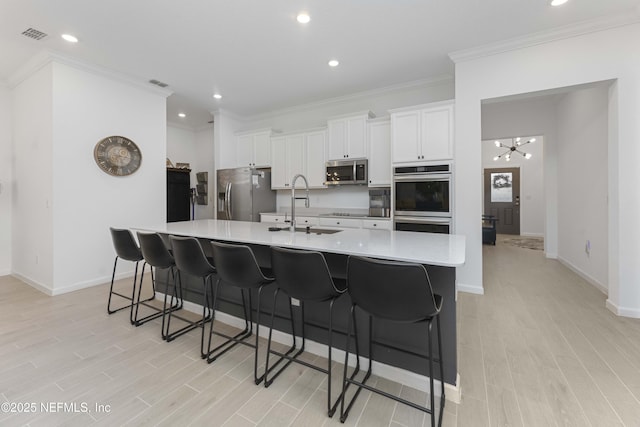 kitchen featuring stainless steel appliances, a spacious island, a notable chandelier, white cabinetry, and sink