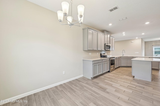 kitchen with gray cabinetry, an inviting chandelier, sink, light hardwood / wood-style flooring, and appliances with stainless steel finishes