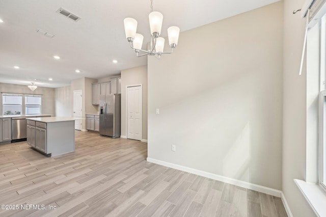 kitchen featuring stainless steel appliances, decorative light fixtures, a chandelier, gray cabinets, and a kitchen island