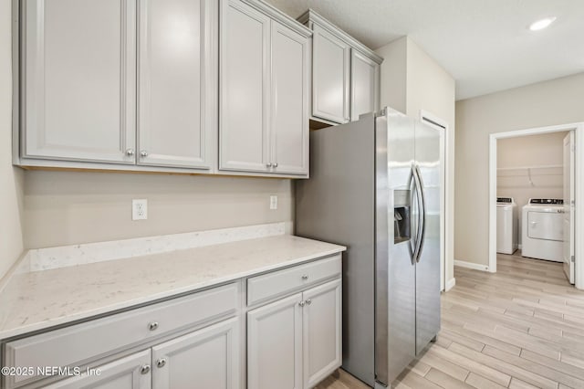 kitchen featuring washer and dryer, light stone countertops, stainless steel fridge with ice dispenser, and light hardwood / wood-style flooring