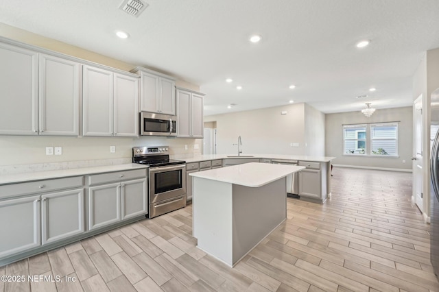 kitchen with kitchen peninsula, appliances with stainless steel finishes, sink, a center island, and gray cabinets