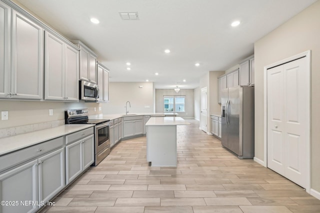 kitchen featuring gray cabinetry, sink, stainless steel appliances, kitchen peninsula, and a kitchen island