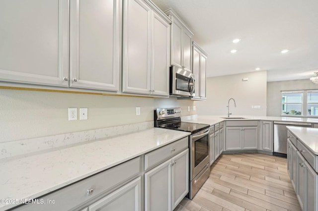 kitchen with stainless steel appliances, light stone counters, gray cabinetry, and sink